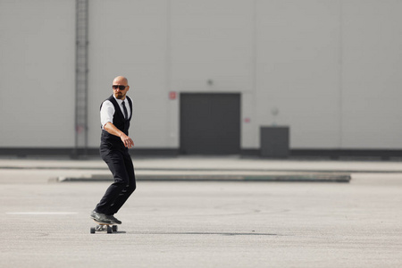 在现代建筑附近的机场长板 skatebourd 的时尚漂亮西装的年轻人