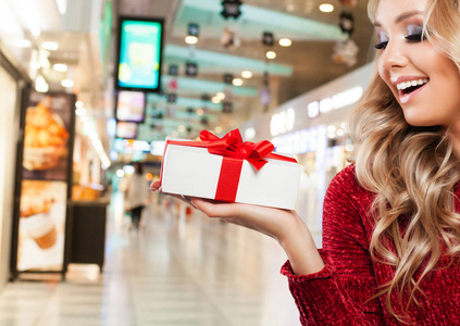笑的女人在圣诞老人帽子与圣诞礼品盒在购物中心背景。圣诞节和新年销售和报价的概念