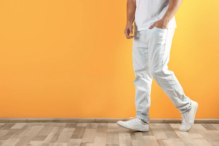 时尚牛仔裤的年轻人在颜色墙壁附近与空间为文本, 焦点在腿