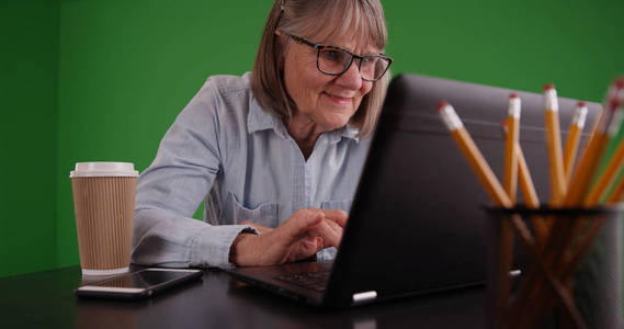 在办公室使用笔记本电脑在绿色屏幕上微笑的老妇人的画像