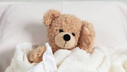 冷烟道或过敏的概念。可爱的泰迪熊躺在床上, 覆盖着温暖的毯子, 拿着一张纸巾