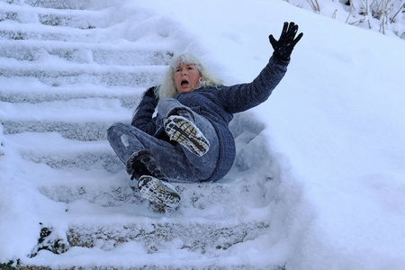 一个女人滑倒在一个寒冷的楼梯上。落在平滑的台阶上