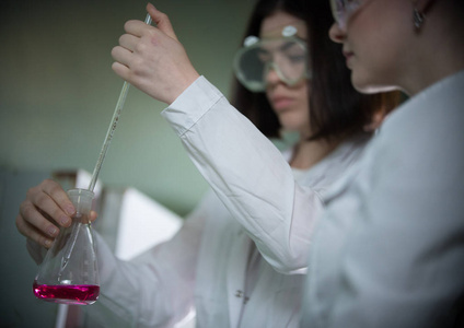 化学实验室。两个年轻女子拿着一个瓶子粉红色的液体在它