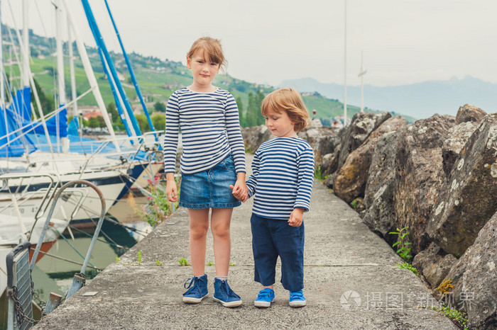 两个时尚的孩子小女孩和男孩穿的连衣裙牵着手在端口玩