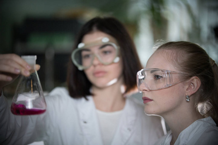化学实验室。两个年轻女子拿着一瓶红色的液体在它看着它