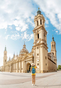 在西班牙阿拉贡萨拉戈萨市的暑假里, 年轻快乐的女子游客在中央广场上著名的德尔皮拉尔大教堂附近散步