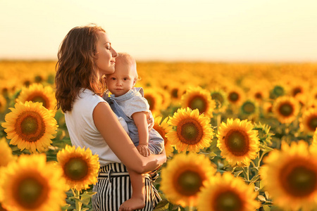 美丽的女人与她的小儿子在向日葵领域在阳光明媚的一天