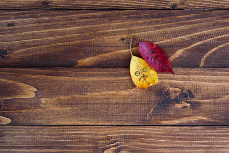 黄色和红色落叶与不同的哀伤的 emoji 表情在木背景