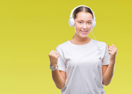 年轻的白种人妇女听音乐戴着耳机在孤立的背景庆祝惊讶和惊讶的成功与双臂举起和睁开眼睛。获奖者概念