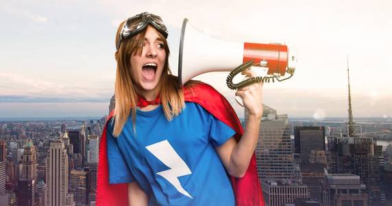 一个漂亮的超级英雄女孩呼喊的扩音器在摩天大楼城市