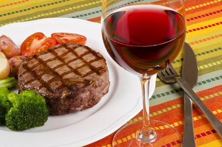 烤的肋眼牛排蔬菜和一杯红酒照片
