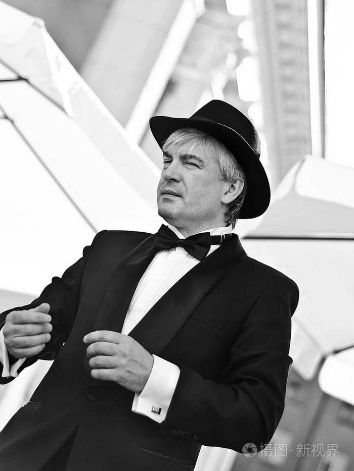 一个灰色头发的老流氓在黑色西装和黑色帽子外从一个不寻常的相机角度