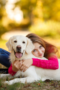 年轻的女孩坐在她的狗猎犬在秋天的场景中与地面上的肖像照片