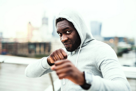 年轻活跃黑人运动员在拳击位置在城市, 佩带帽衫