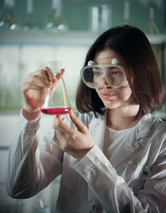 化学实验室。工作眼镜的年轻妇女看着烧瓶