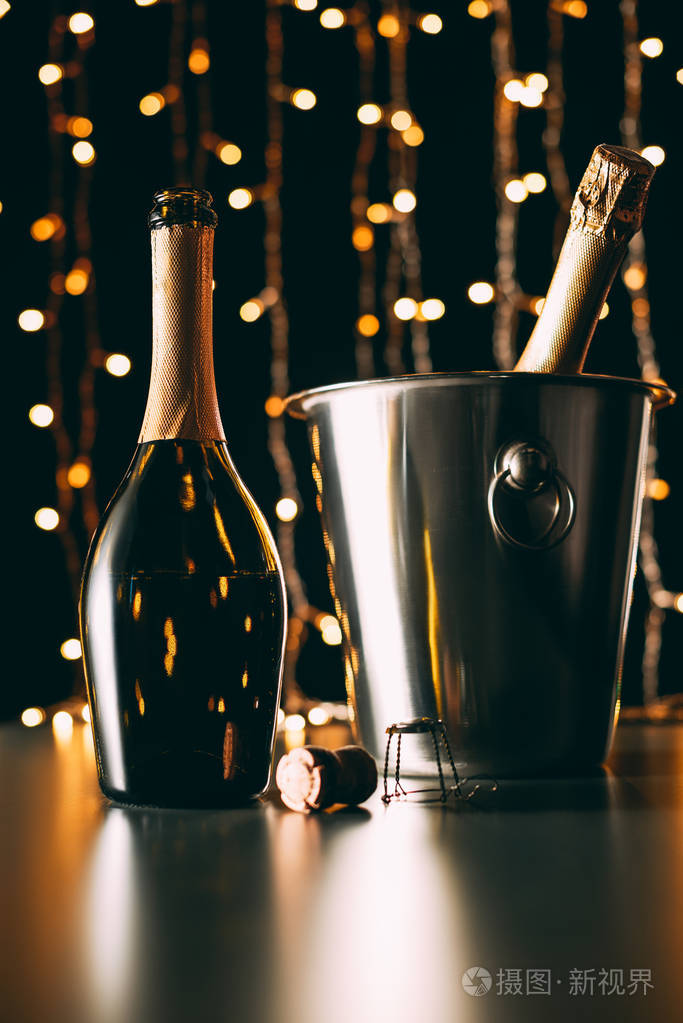 香槟瓶在桌上和桶上的瓶子在花环浅色背景, 圣诞节概念