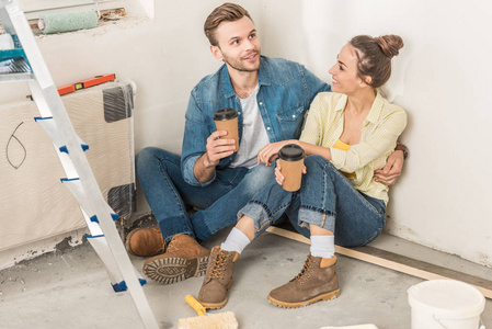 在新公寓里, 微笑的年轻夫妇拿着纸杯, 坐在地板上的高角度的看法