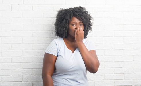 年轻的非洲裔美国人加大小的妇女在白色砖墙看紧张和紧张与手在嘴咬指甲。焦虑问题