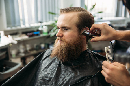头发削减主削减头发和胡须的男子在理发店,理发师使发型对于一个年轻