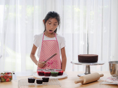 快乐的亚洲女孩学习如何在家里做纸杯蛋糕, 生活方式的概念