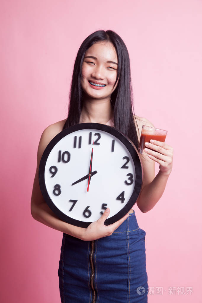 年轻的亚洲妇女与蕃茄汁液和时钟在粉红色背景