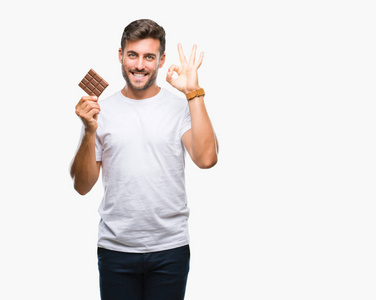 年轻英俊的男人吃巧克力棒在孤立的背景做确定的标志与手指, 优秀的象征