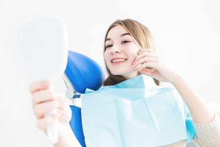 牙科诊所。接待, 检查病人。牙齿护理。年轻女孩微笑着, 看着镜子后, 她的牙医牙科检查