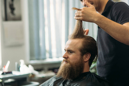 年轻理发师的手理发到有吸引力的胡子男子在理发店