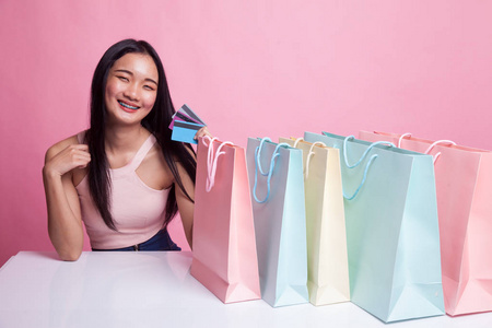 年轻的亚洲妇女与购物袋和空白卡粉红色背景
