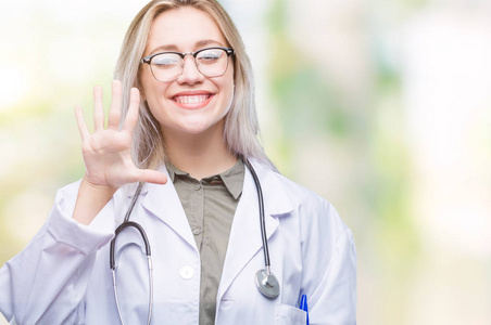年轻的金发碧眼的医生妇女在孤立的背景显示和指向与手指数字五, 而微笑着自信和快乐