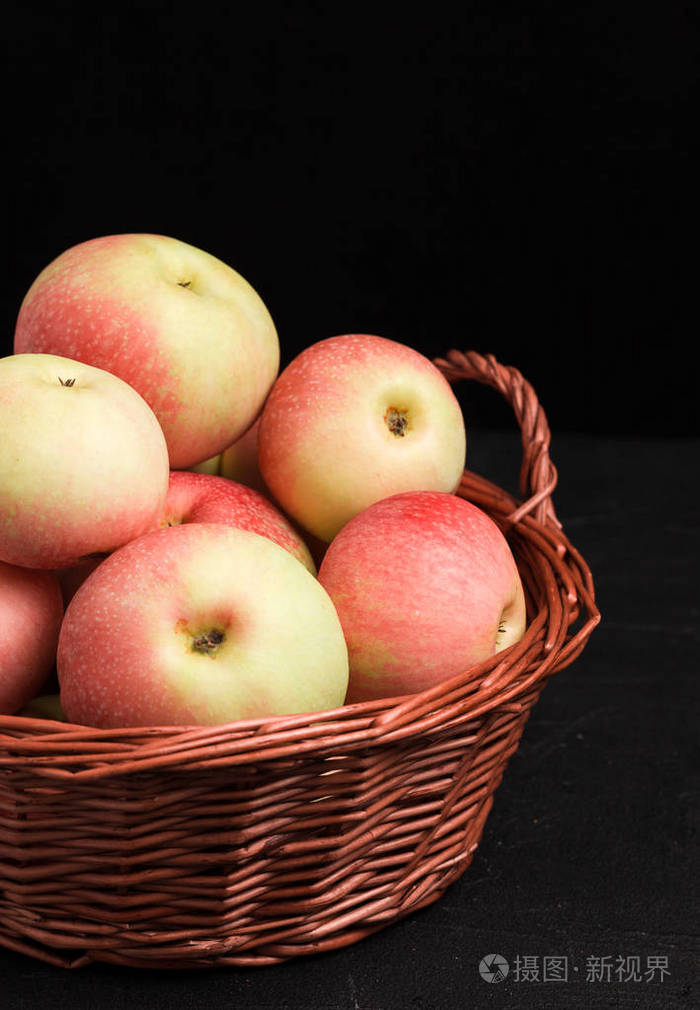 成熟的原始苹果在柳条篮子在黑色背景与拷贝空间垂直横幅与有机农场