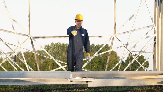 一名电工或建筑工人, 身着蓝色长袍的员工, 身穿黄色头盔, 准备安装电线杆电塔和能源