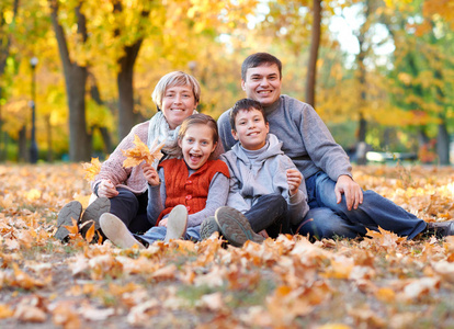 愉快的家庭在秋天城市公园在落叶说谎。孩子们和家长摆姿势, 微笑, 玩耍和娱乐。明亮的黄色树