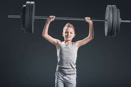 前青春期男孩的肖像在运动中举行杠铃在黑暗的背景照片
