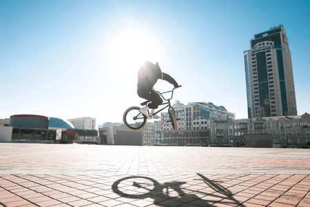 街道上的一个 bmx 骑手在城市景观和阳光的背景下跳在大街上的肖像。bmx 概念。bmx 上的街头自由泳