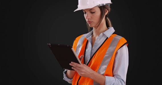 在橙色背心和安全帽工作在平板电脑上的固体灰色背景的妇女