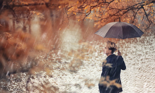 秋天下雨的天气和一个年轻的人用雨伞