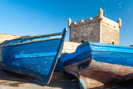 两艘蓝色渔船搁浅在摩洛哥莫加多尔城堡脚下的码头上。