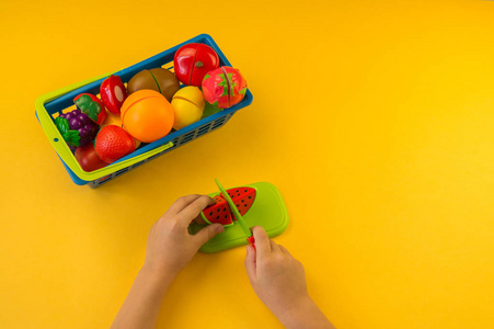一个孩子在木板上切一个塑料水果。孩子们的手。玩厨师。黄色背景