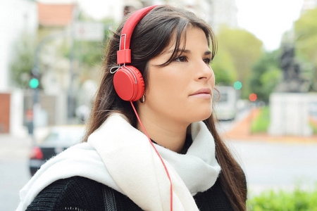 年轻漂亮的女人，戴着红色耳机听音乐的画像。户外活动。城市概念