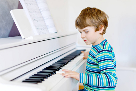 漂亮的小小孩男孩戴着耳机在客厅或音乐学校钢琴。学龄前儿童开心学习演奏乐器。教育，技能的概念