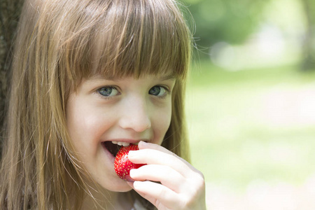 小可爱的女孩与美丽的脸享受, 而吃一个多汁的草莓。为您的文本提供空白空间