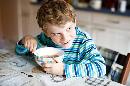 可爱的金发碧眼的小男孩在早餐或午餐吃麦片粥和牛奶和浆果。儿童健康饮食, 学童。在学校食堂或在家