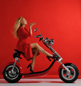 妇女骑新电动车摩托车自行车滑板车礼物新的年2019在红色礼服吹亲吻与嘴唇上红色的符号