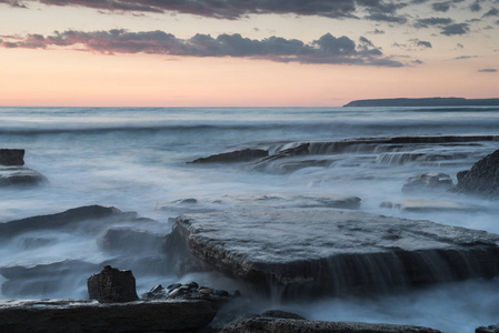 在位于塞浦路斯利马索尔阿克罗蒂里地区的岩石上, 巨浪般的日落在岩石海岸上。长曝光摄影