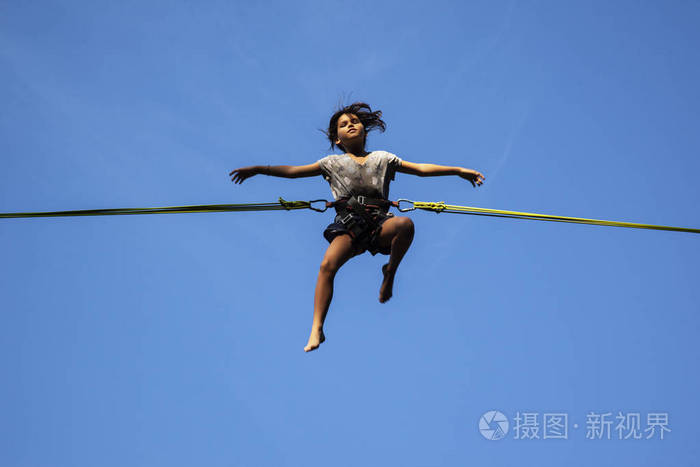 小女孩有乐趣在绳索跳跃以蓝色天空在背景上
