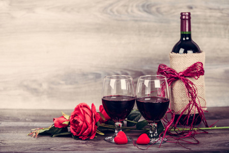 红酒瓶, 两杯葡萄酒, 玫瑰与装饰红心在木桌上。情人节庆祝概念。复制空间