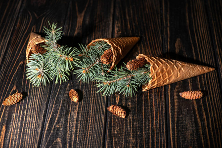 一个三个华夫饼锥与圣诞树的 sprigs 躺在黑暗的木头上, 复制空间摄影