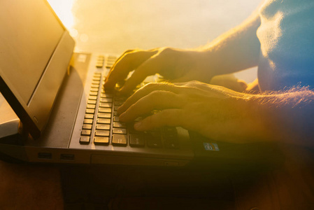一个男人在他的笔记本电脑键盘上的文字在河边的日落时打字。那家伙忙于工作