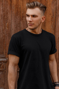 时髦的男人与时尚的发型在时尚的黑色模型 t恤站在木复古门附近